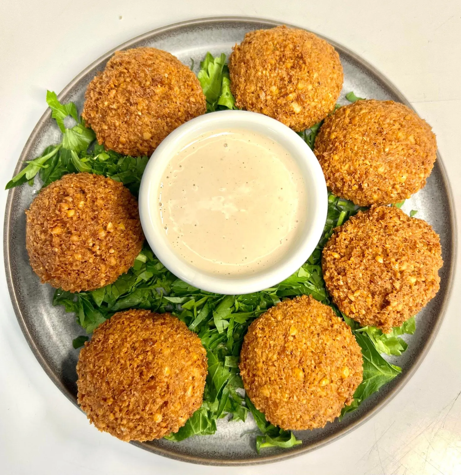 Seks falafel rundt en skål med tahinisaus på salatblader