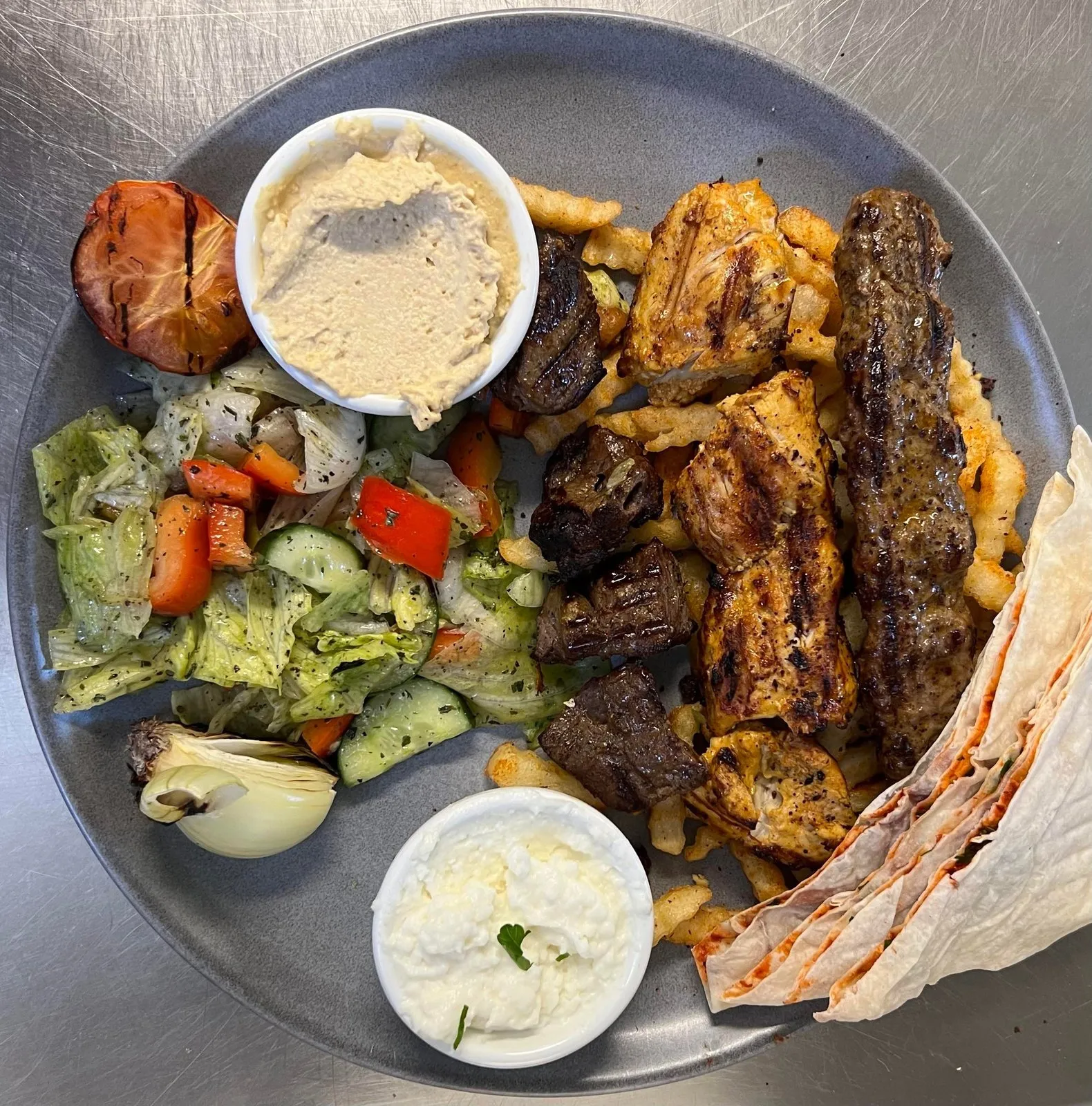 Tallerken sett ovenfra med grillet kjøtt og kylling, salat, hummus, hvitløkssaus og brød